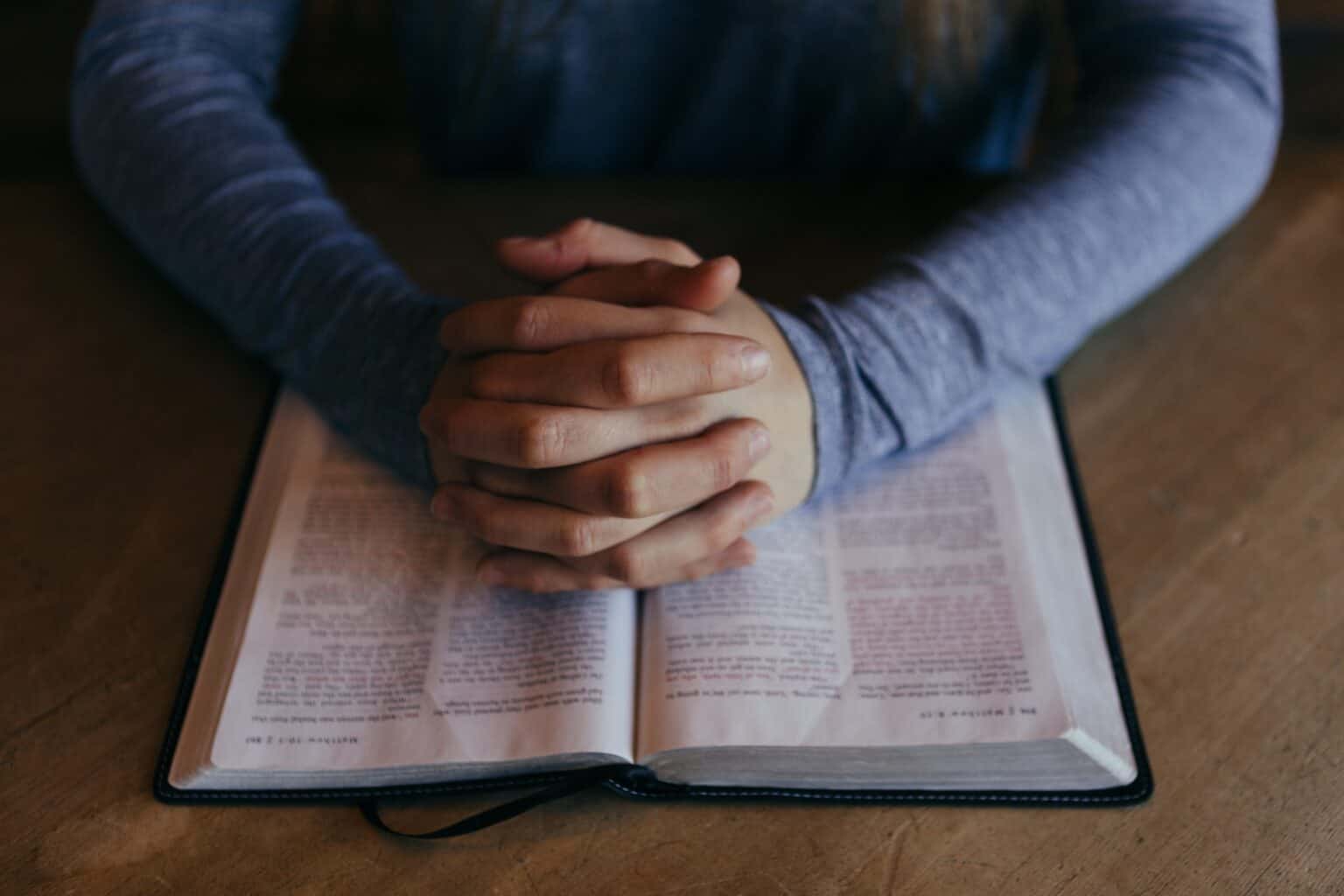 praying hands resting on top of an open bible